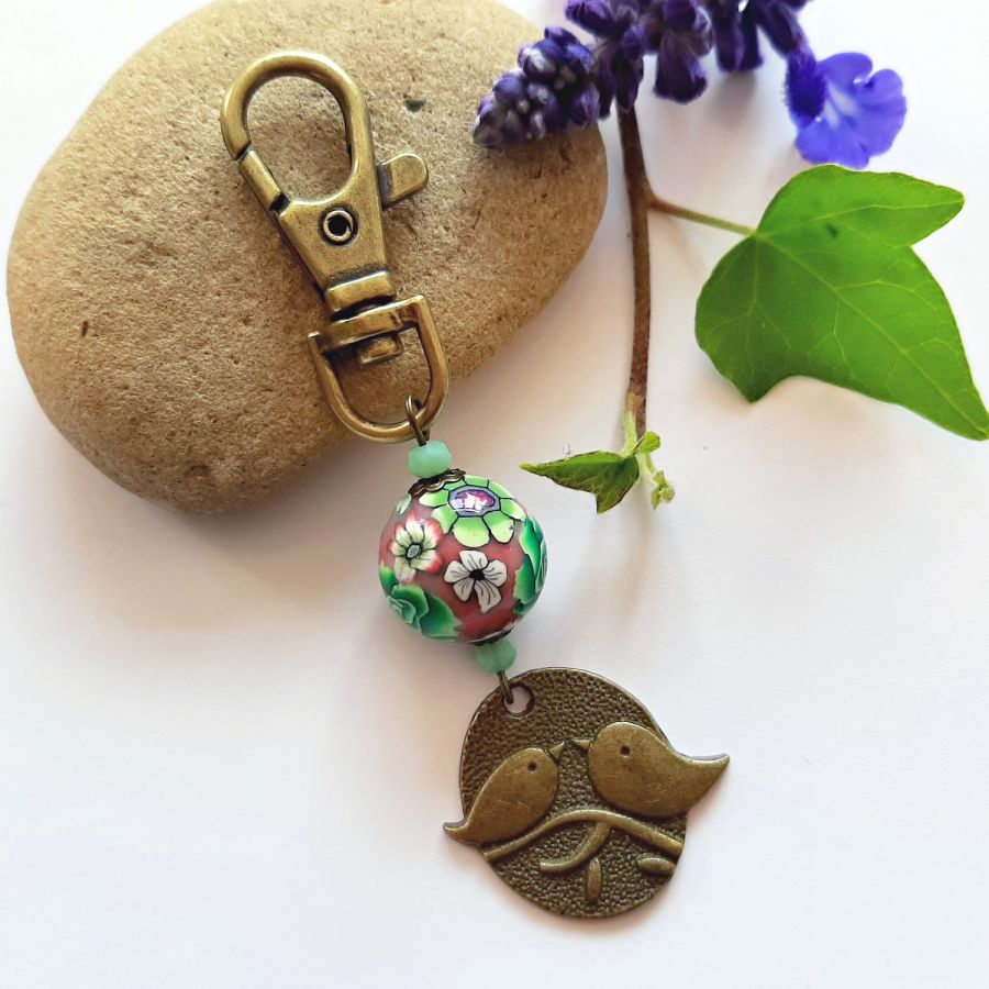 chaveiro medalha duo de pássaros cor bronze e pérola floral trabalhada motivo floral verde e vinho leesmulticolour