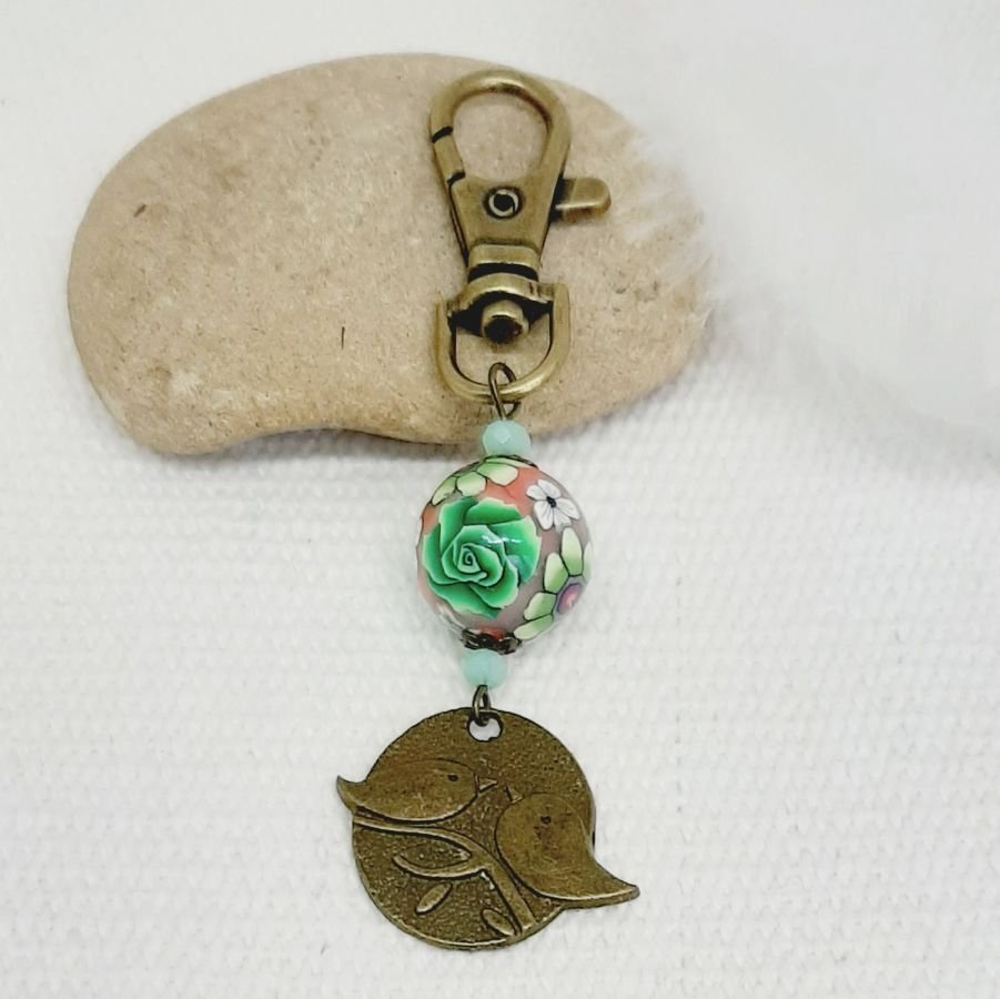 chaveiro medalha duo de pássaros cor bronze e pérola floral trabalhada motivo floral verde e vinho leesmulticolour