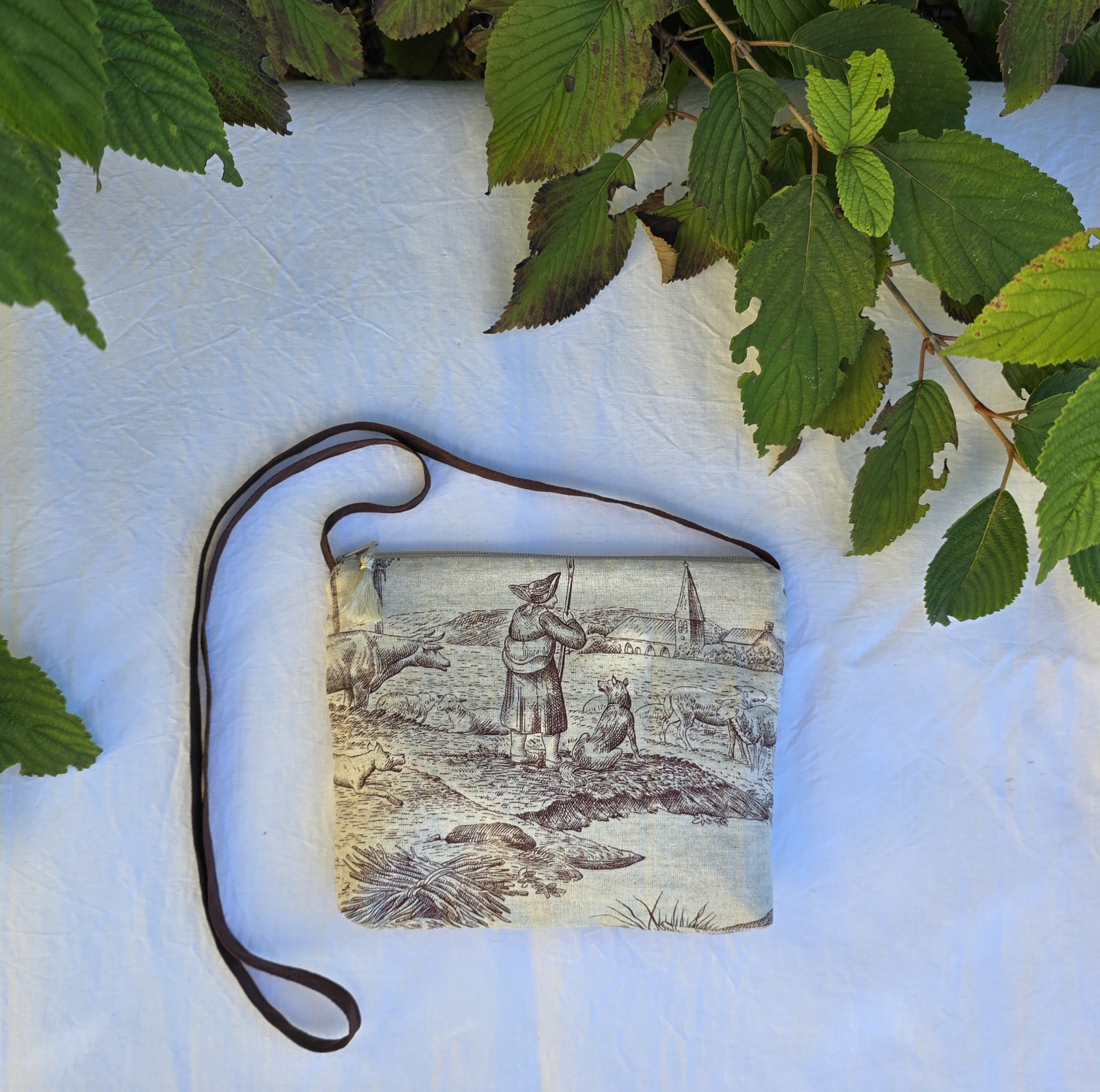 Pochette avec bandouli&egrave;re en tissu toile de Jouy marron et beige agr&eacute;ment&eacute;e d'un pompon