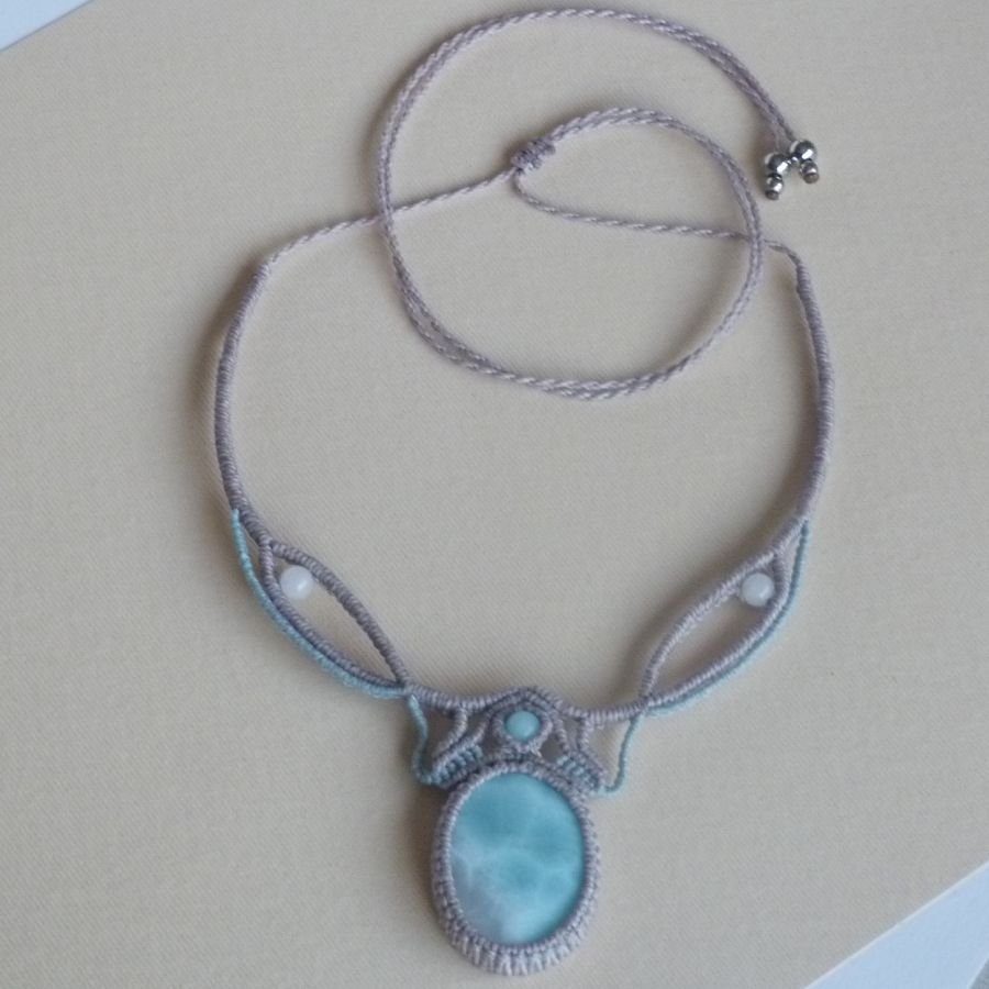 Colar em micro-macramé cinzento-acinzentado/azulado fosco com uma pedra preciosa natural em tons suaves de branco e azul claro como peça central.