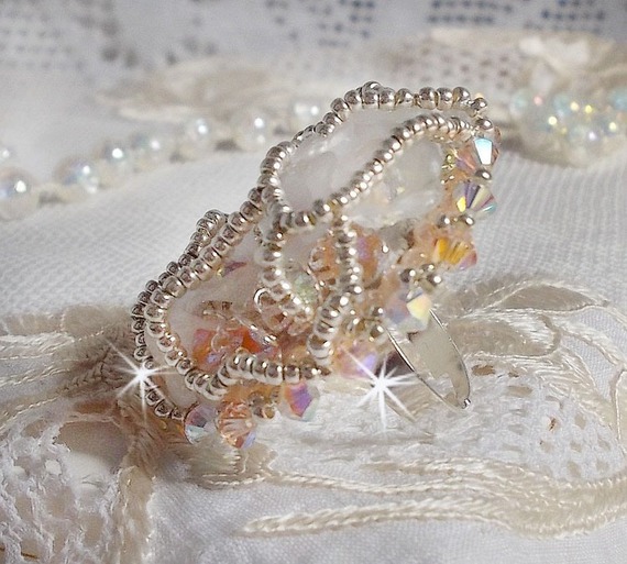 Anel Bouquet d'un Jour bordado com lírios de lucite, topos giratórios de cristal Swarovski, um cabochon perolado com missangas de prata e salmão
