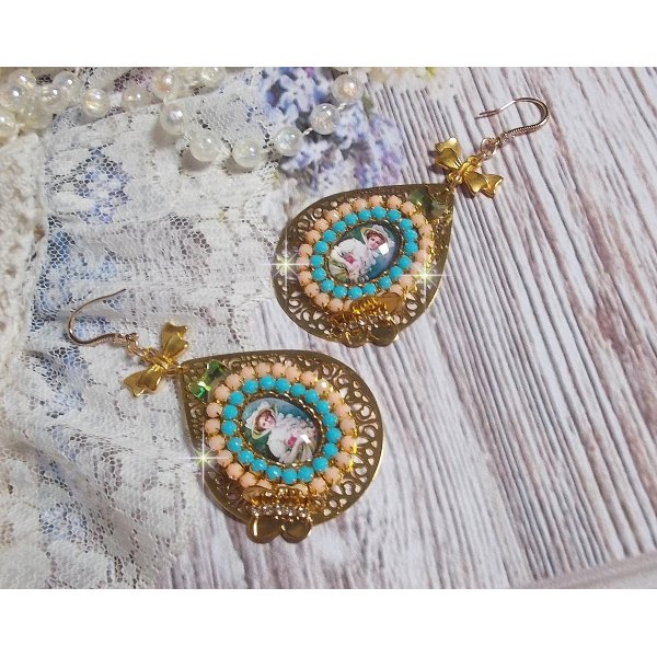 BO Mademoiselle Noellia avec des cabochons ovales repr&eacute;sentant une femme avec un chapeau et un n&oelig;ud blanc &agrave; laquelle s&rsquo;ajoute des cristaux, cha&icirc;nes strass P&ecirc;che et Turquoise sur crochets en plaqu&eacute; Or