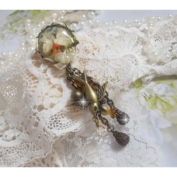 Broche Colombes aux plumages blancs avec des breloques filigran&eacute;es gouttes et lisses, perles rondes et n&oelig;ud en cristal, ruban organza cr&egrave;me, pendentif plaqu&eacute; or avec un zircon sur une broche en m&eacute;tal
