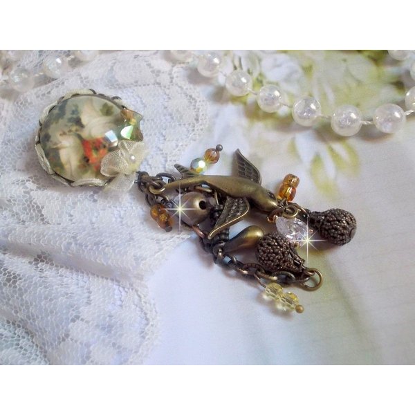 Broche Colombes aux plumages blancs avec des breloques filigran&eacute;es gouttes et lisses, perles rondes et n&oelig;ud en cristal, ruban organza cr&egrave;me, pendentif plaqu&eacute; or avec un zircon sur une broche en m&eacute;tal