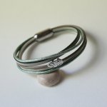 Pulseira multi-couro em tons de bege, verde pálido e perolado, decorada com uma pequena pena